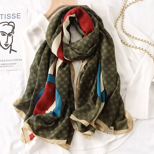 Detail of olive green scarf with vintage monogram pattern on white shirt and wood hanger