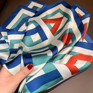 Close-up of a smooth silk-like scarf with modern colorful geometric print held by hand