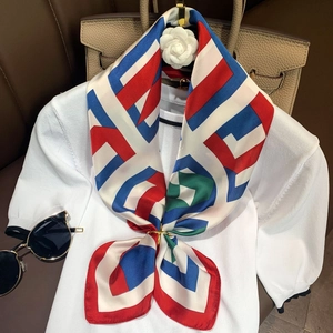Detail of geometric print silk scarf with a gold ring buckle on a white knit top