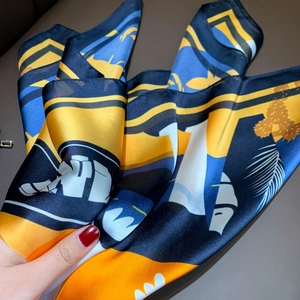 Close-up of a glossy satin scarf with navy and yellow geometric tropical prints
