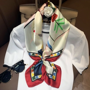 Detailed shot of printed silk scarf with floral patterns and pearl buckle on white knitwear