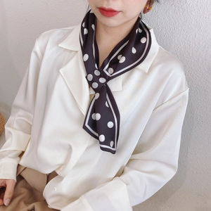 Gros plan d'un foulard étroit en soie à pois blancs noué sur le col d'une chemise beige