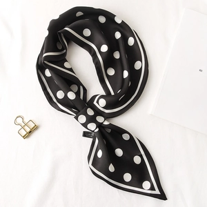 Gros plan d'un foulard en soie à pois noirs et blancs avec une pince dorée élégante