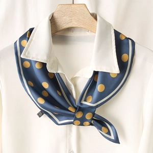 Détail d'un foulard en soie à pois bleu marine noué sur une chemise blanche satinée
