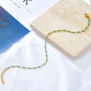 Detail of gold ankle chain with green enamel beads on a textured stone surface