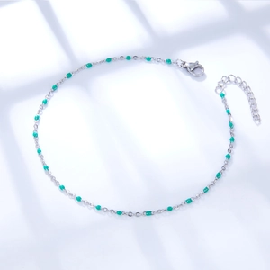 Silver chain anklet with green beads and butterfly charm detail on a blue background