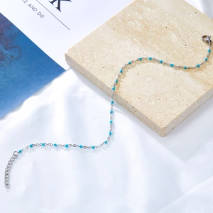 Detail of silver chain anklet with sky blue enamel beads on a textured stone surface
