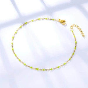 Detail of gold ankle chain featuring vibrant neon green enamel beads and lobster clasp