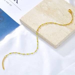 Detail of gold chain anklet with neon green beads and lobster clasp on silk