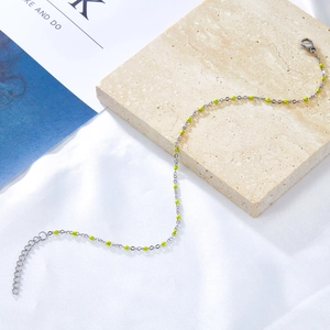 Detail of silver stainless steel anklet with neon green beads on textured stone surface