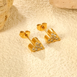 Elegant gold heart stud earrings with white rhinestones on stones and beige surface
