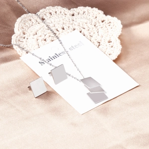 Macro view of polished stainless steel square pendant and earrings on satin background