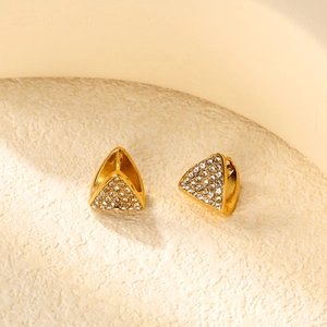 Goldene geometrische Dreiecksohrringe mit weißem Kristallpavé auf Steinhintergrund