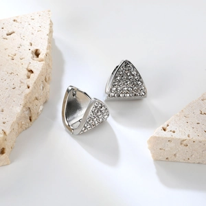 Détail de créoles triangulaires argentées avec strass blancs sur fond de pierre