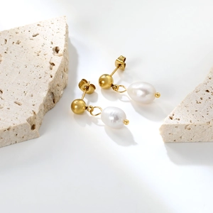 Elegant gold ball stud earrings with freshwater pearl drops on minimalist stone display