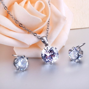 Macro view of six-prong silver necklace and matching stud earrings set on rose petals