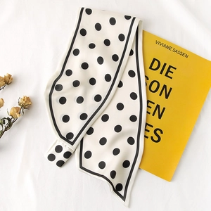 Vue détaillée de l'écharpe étroite en soie à pois avec bordure noire sur livre jaune
