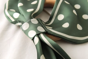 Détail d'un foulard en soie vert foncé à pois avec texture satinée et anneau en bois