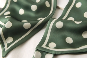 Gros plan sur le foulard en satin vert foncé à pois avec texture lisse et bords ourlés