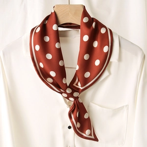 Gros plan d'un foulard en soie à pois caramel noué sur une chemise blanche chic