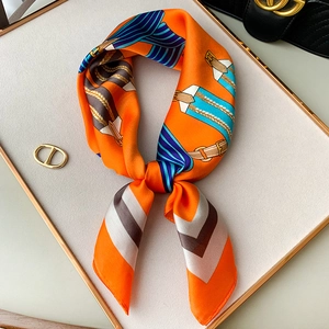 Elegant orange silk square scarf with horse bridle print on luxury display tray