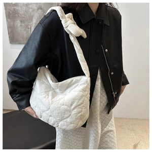 Detail of white quilted canvas shoulder bag with unique knot strap design on model