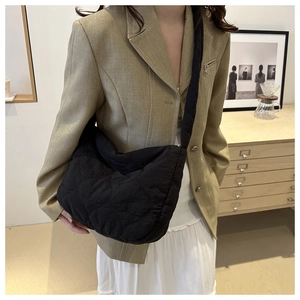 Detail of black quilted puffer crossbody bag worn with a casual blazer on a shoulder