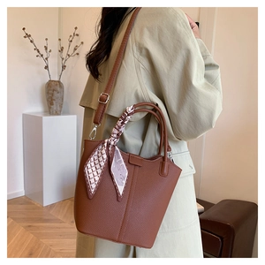 Brown lychee leather bucket bag detail with decorative silk scarf and adjustable strap