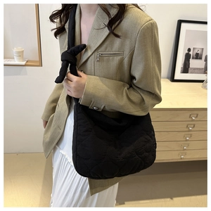 Detail of black heart-quilted canvas shoulder bag with wide knotted strap on model