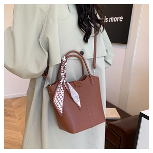 Detail of a brown lychee-patterned bucket bag with decorative scarf on the handle
