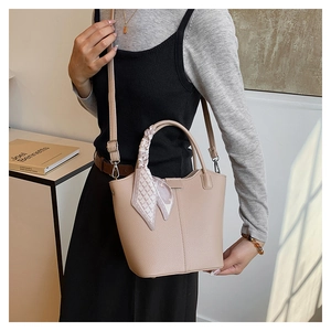 Close-up of beige lychee texture bucket bag with decorative silk scarf on handle