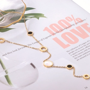 Detail view of a long gold tassel necklace with black enamel and white shell round pendants