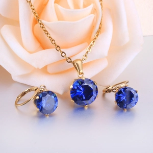 Elegant six-prong gold jewelry set with blue round crystals on a reflective surface