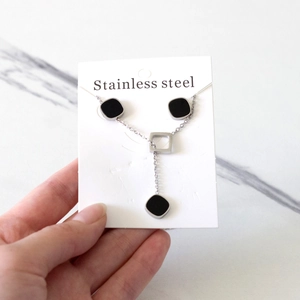 Detail of stainless steel necklace featuring black square pendants on marble background