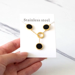 Detail of a gold stainless steel necklace featuring black shell disc pendants on a card