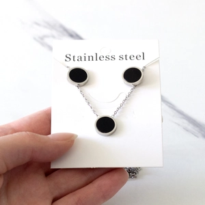 Detail of minimalist stainless steel jewelry set with black round geometric pendants