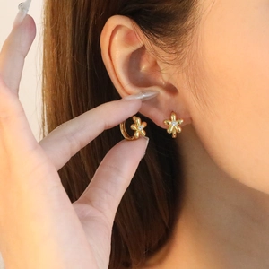 Gros plan de boucles d'oreilles fleur dorées avec zircon blanc portées par un mannequin