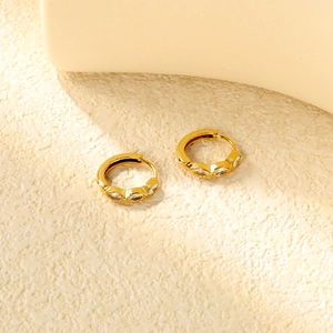 Détail de boucles d'oreilles créoles dorées ornées de trois zircons blancs marquise