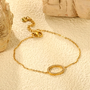 Detail of gold chain bracelet with CZ paved circle charm on a textured stone surface