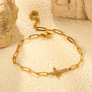 Macro detail of golden cross bracelet with zircon inlay on a textured stone surface