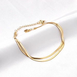 Double-layered gold flat snake chain anklet with heart pendant on white silk fabric