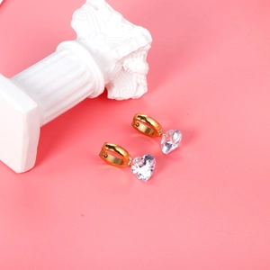 Detailed view of heart-shaped crystal earrings with golden hoops on a pink background
