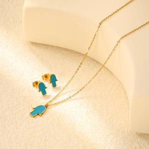 Détail d'une parure Hamsa dorée avec émail turquoise sur un présentoir blanc