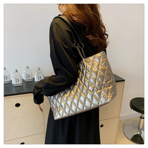 Quilted silver tote bag with metallic finish and chain strap worn by a model in a home setting