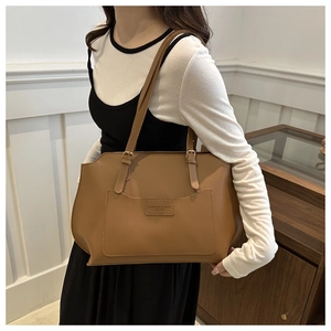 Détail du sac cabas marron avec écusson en cuir embossé et boucles dorées sur la bandoulière