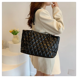 Detail of black quilted puffer tote bag with chain strap worn by a model in a minimal studio