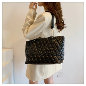 Detail of black quilted tote bag with golden chain straps and high-gloss finish texture