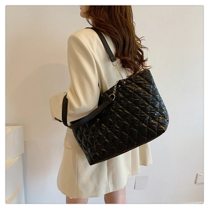 Detail of black quilted puffer tote bag with chain strap shown on model shoulder
