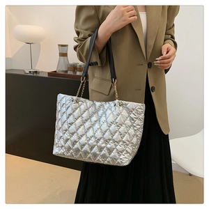 Silver quilted tote bag with chain straps worn by a model in a minimalist modern room