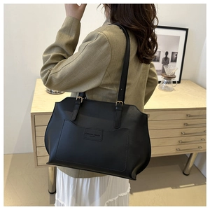 Close-up of black leather tote bag with embossed text and long shoulder straps worn by model